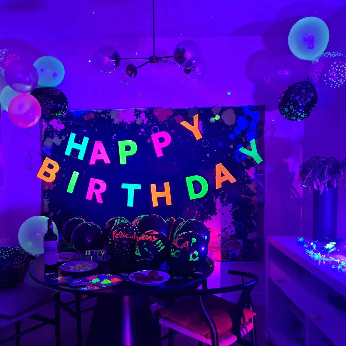 Mesa de cumpleaños con globos pintados y guirnalda de letras fluorescentes