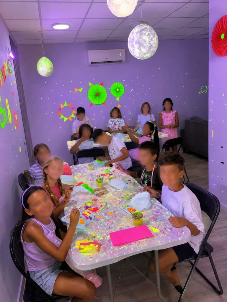 Niños pintando bolsas de tela con colores alrededor de la mesa del taller